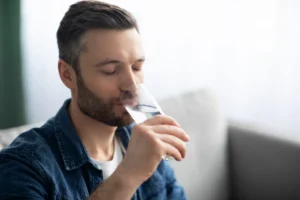 śmiechnięty, brodaty mężczyzna w dżinsowej koszuli pije orzeźwiającą szklankę czystej wody Culligan w jasnym pomieszczeniu.